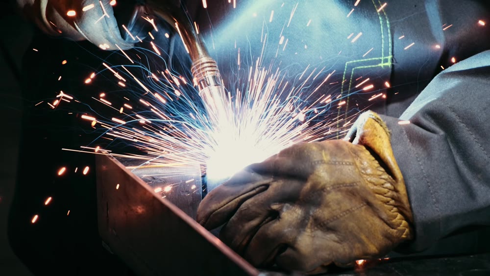Close-up of a blacksmith welder working with metal using a welding machine, bright sparks and flashes in slow motion
