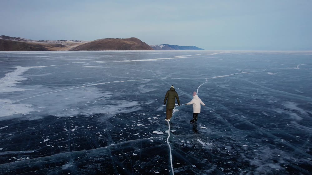 A man-father with a little girl-daughter is skating on the blue transparent ice of the boundless Lake Baikal. Unique places on earth.